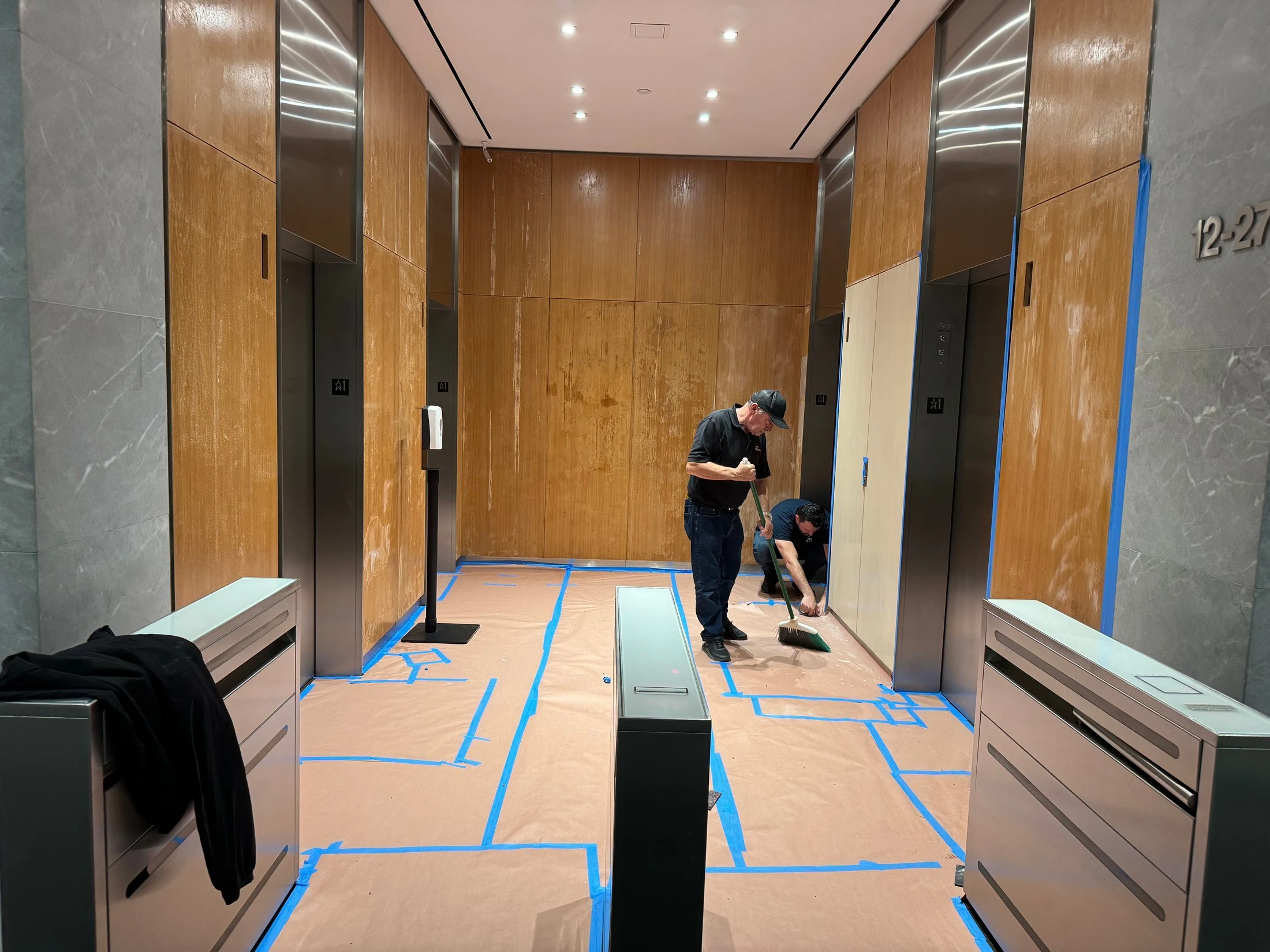 Wood elevator-lobby panels before restoration, with Luxor technicians at work